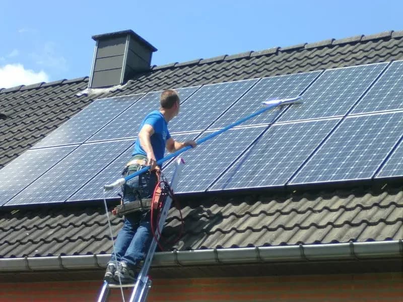 Personne effectuant le nettoyage d'un panneau solaire à l'aide d'une brosse et d'eau, illustrant l'entretien régulier nécessaire.